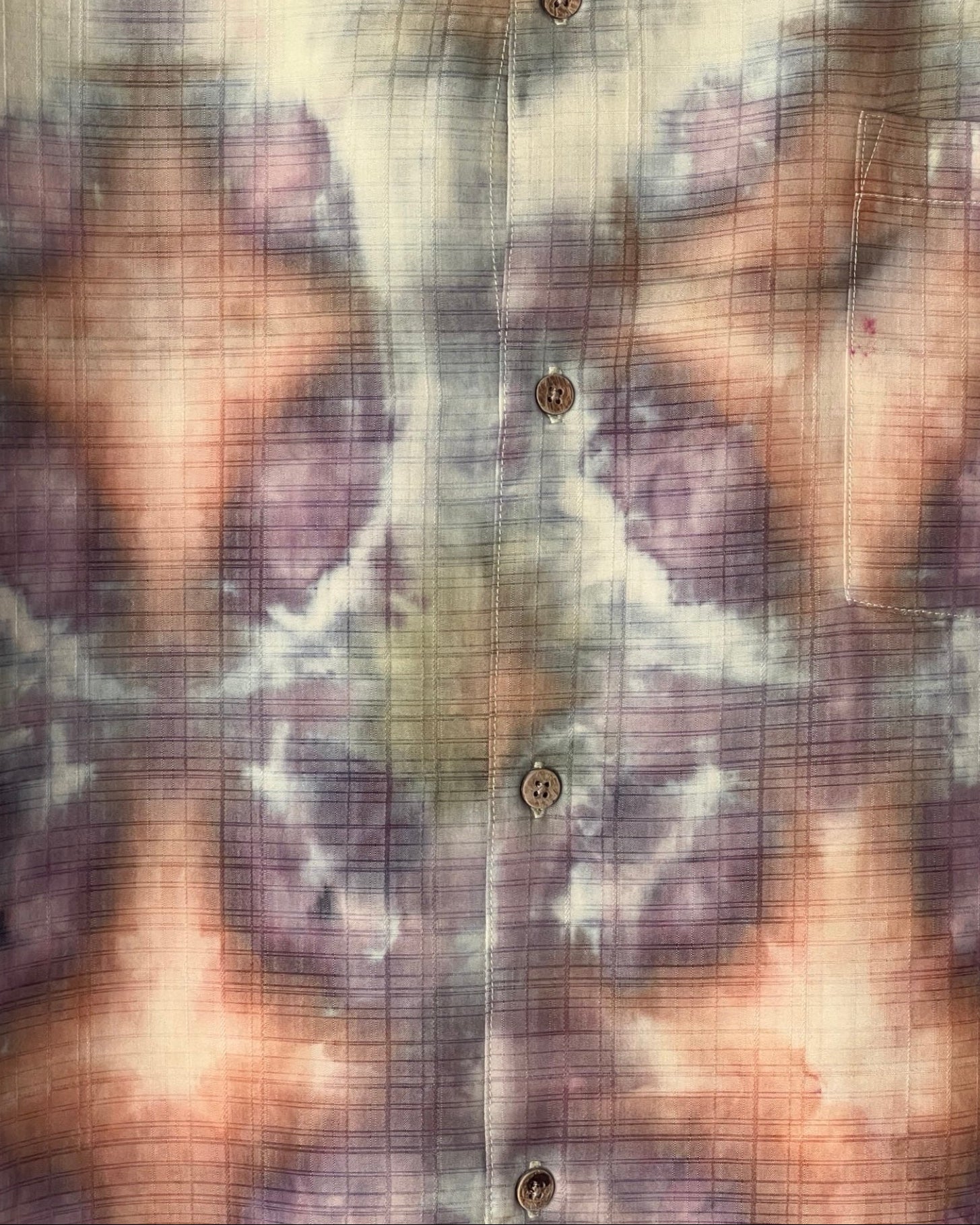 Close-up of a tie dyed shirt with abstract designs in brown, purple, and beige.