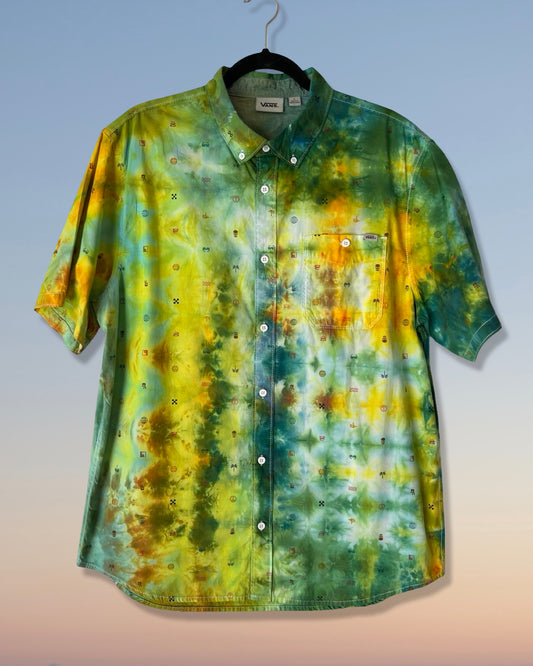 Tie-dye shirt with green, yellow, and brown patterns on a hanger against a gradient background.