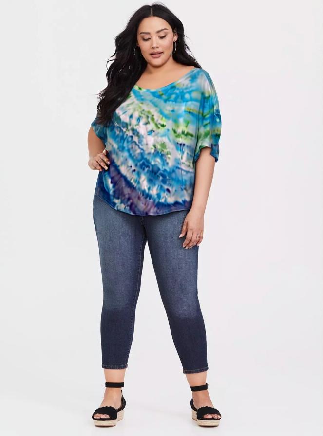 Woman wearing a blue tie-dye top and blue jeans on a white background