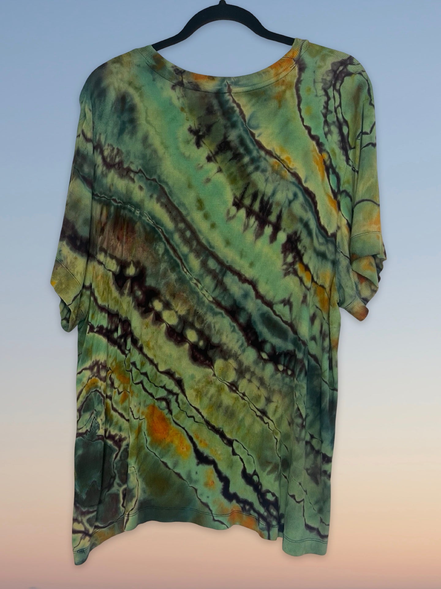 Tie-dye shirt on a hanger with a gradient of green, brown, and orange colors.