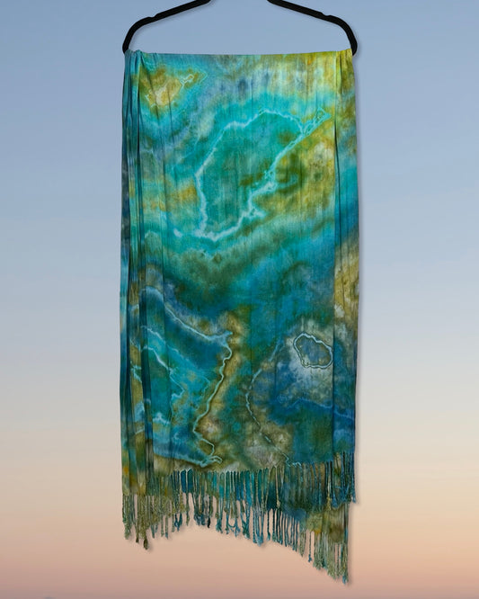 Scarf with a green and blue pattern on a hanger against a gradient background